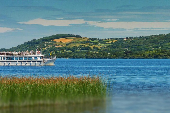 Boat on lake with grassy shore, hills in background.