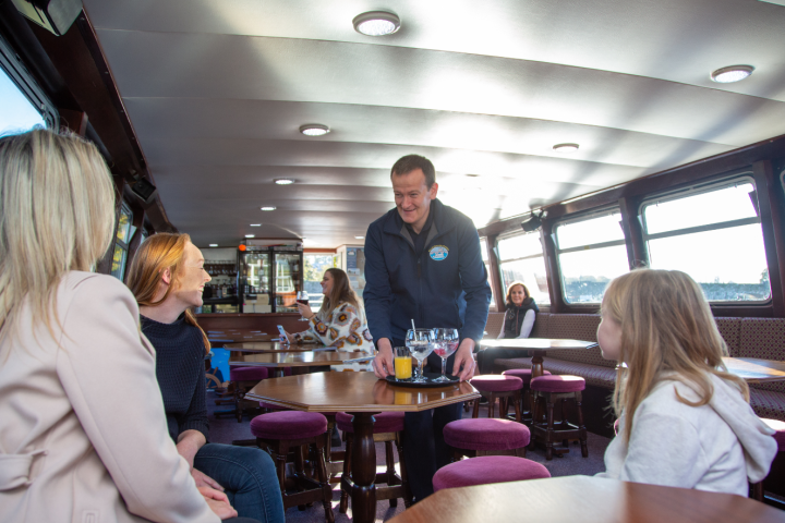 Waiter serves drinks to three people sitting at a table on a boat.
