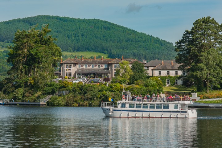 Boat on a lake with a hillside hotel and greenery in the background.