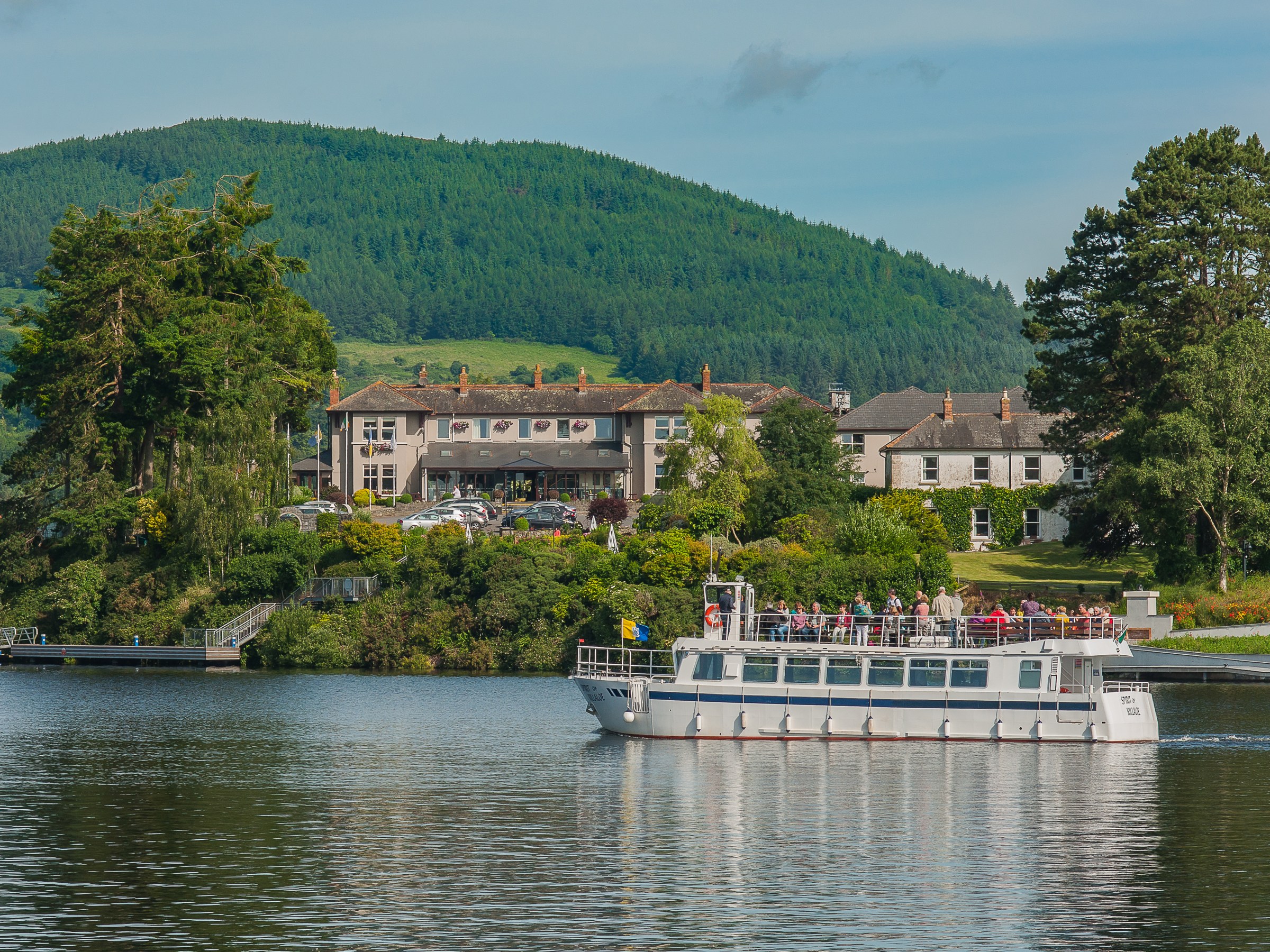 Tour boat on lake with tree-covered hill and a building in the background.