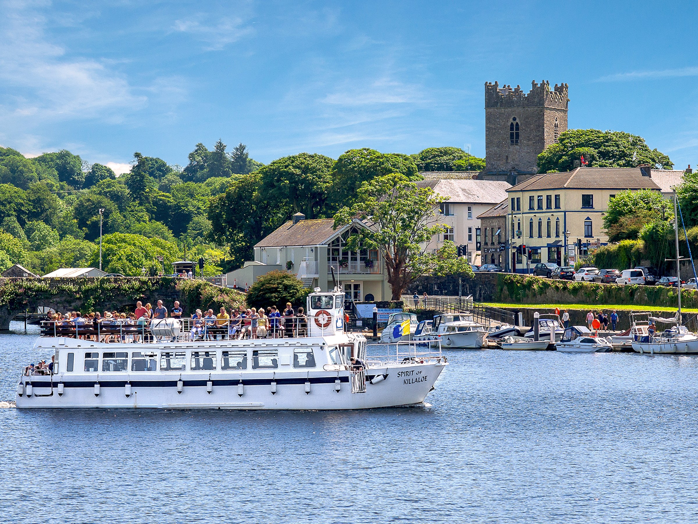 White tour boat on river with buildings and trees in background.