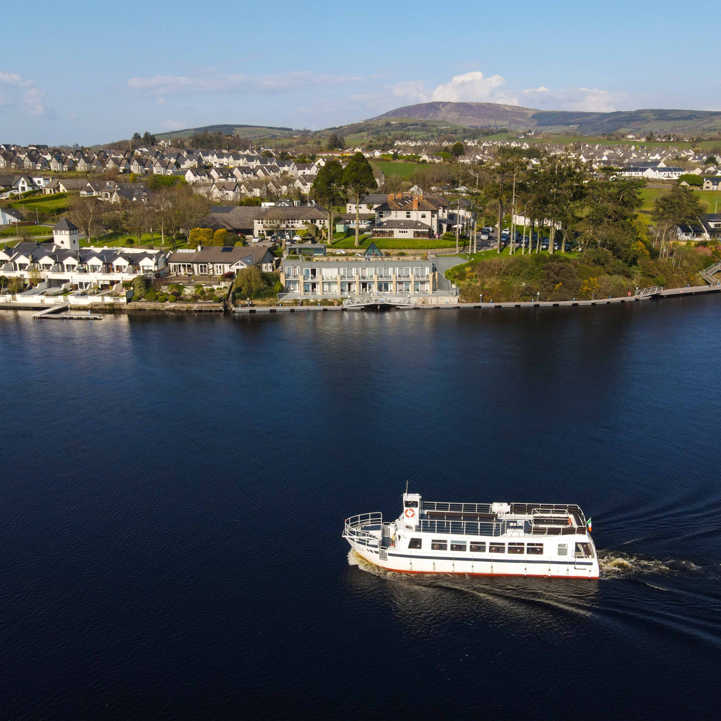Boat on a calm lake with houses and trees on the shoreline, under a clear blue sky.