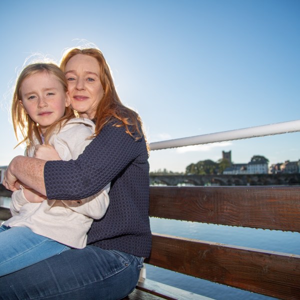 Woman hugging child on a sunny bench with a river view.