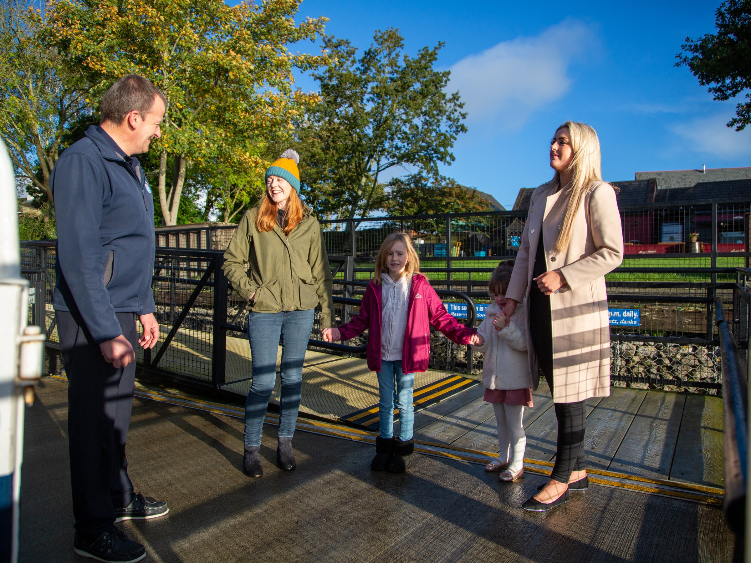 Four people and a child talking outdoors on a sunny day, with trees and buildings in the background.