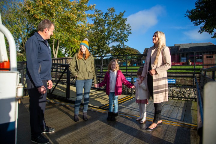 Four people and a child talking outdoors on a sunny day, with trees and buildings in the background.