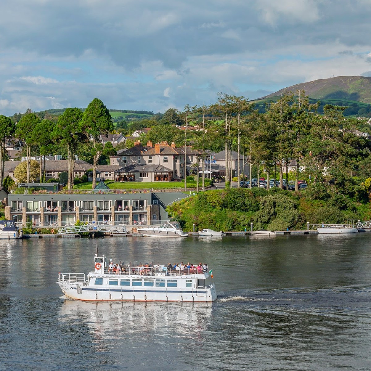 Tour boat on river with houses and hills in the background under a cloudy sky.