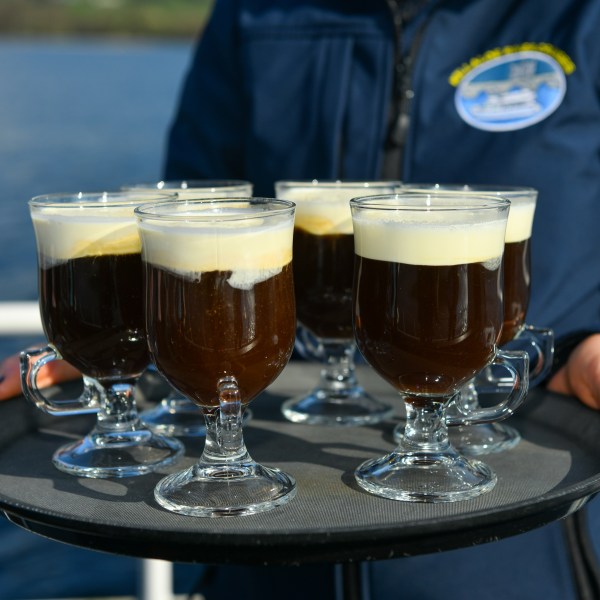 Person holding tray with six Irish coffee drinks by the water.