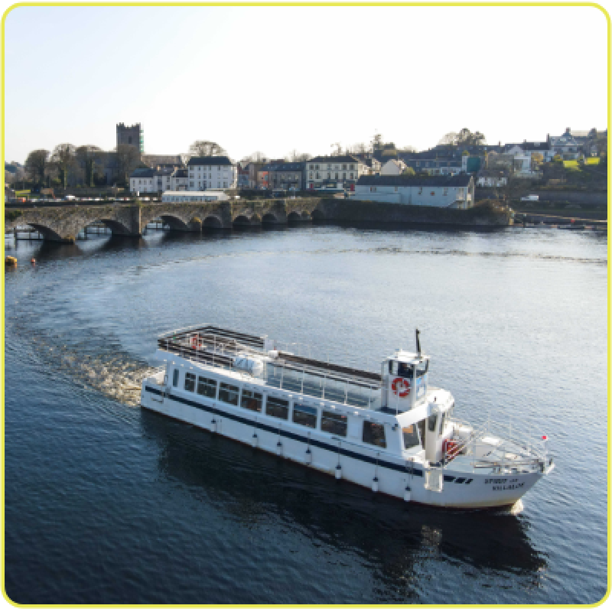 White ferry on river with arched bridge and town in background.