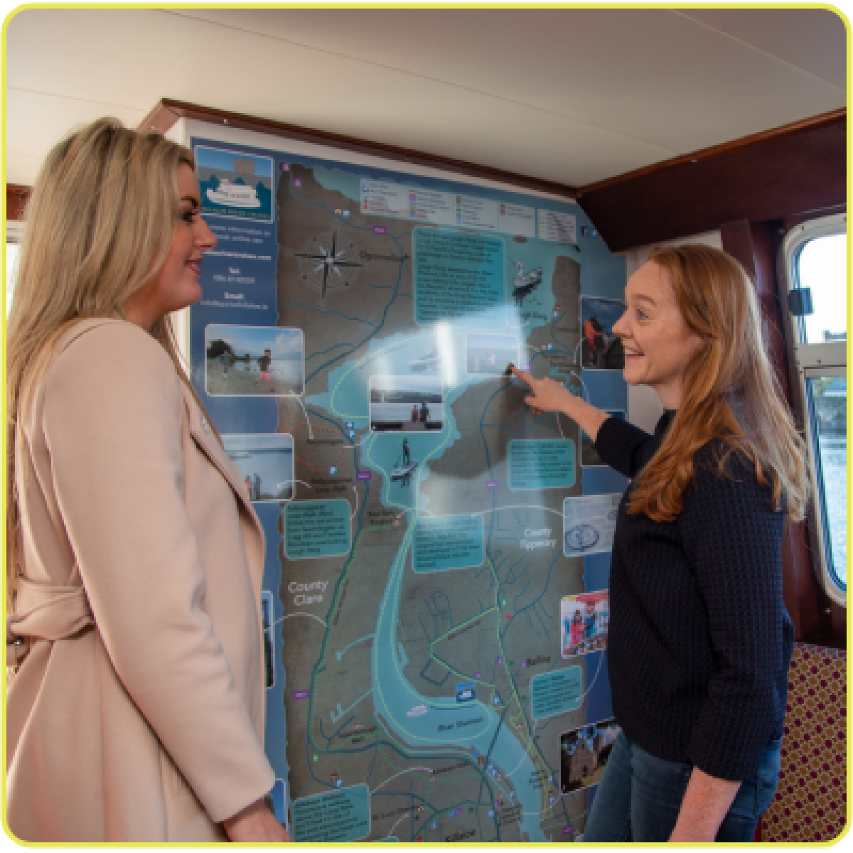 Two women discussing a map on a wall on a boat.