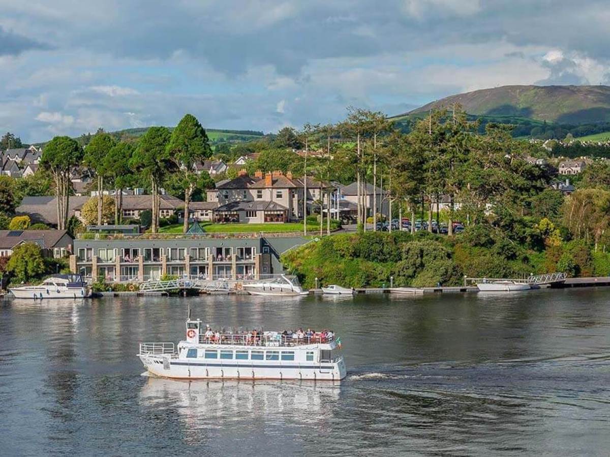 Tour boat on river with houses and hills in the background.