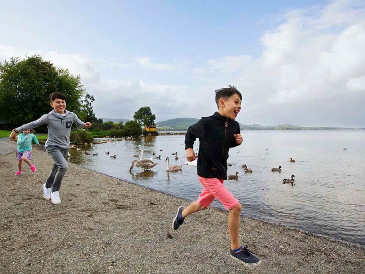 Three children joyfully running along a lakeside path.