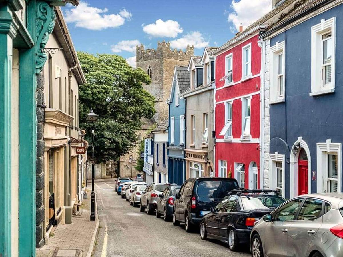 Colorful houses on a narrow street with parked cars and a church in the background.