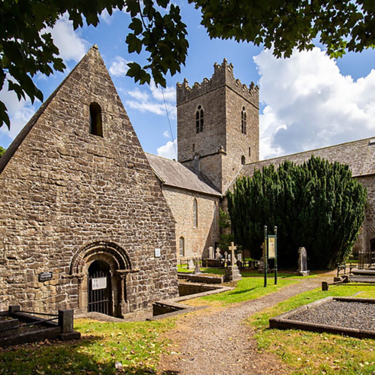 Stone church with arched entrance, tower, and gravestones under a partly cloudy sky.