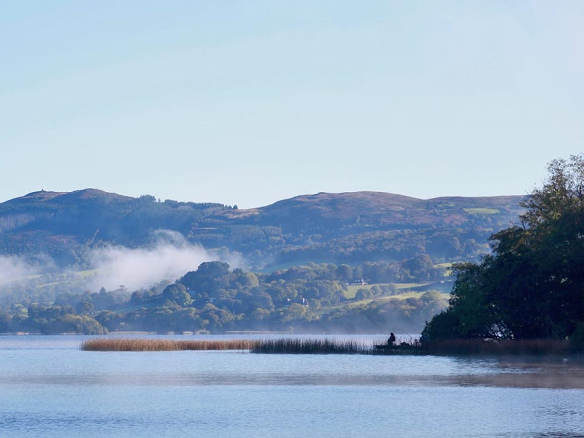 Serene lake with mist, mountains, and trees in the background.